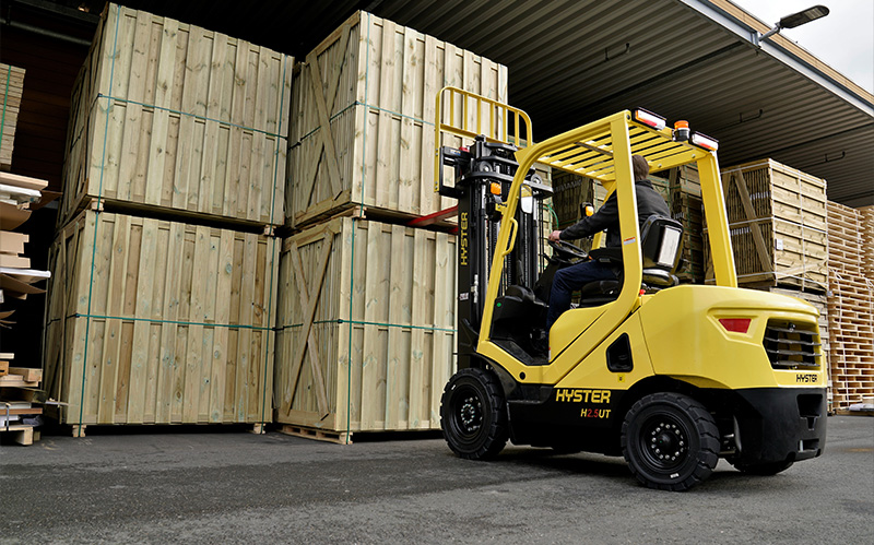 Yellow diesel counterbalance forklift stacking large wooden crates outdoors