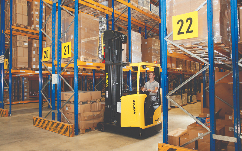 Southeast Asian warehouse worker connecting an electric forklift to a lithium-ion charging station in a modern Singapore warehouse with tall storage racks and pallets.