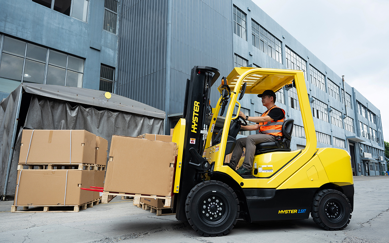 Operator-driving-a-yellow-Hyster-forklift-outdoors-with-cargo-1