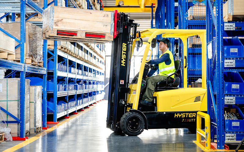 Operator-driving-a-yellow-Hyster-forklift-outdoors-with-cargo
