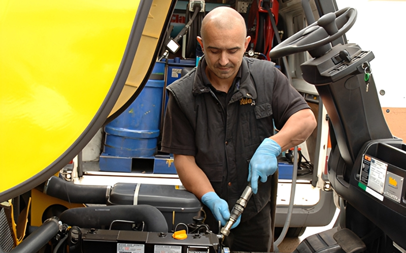 Forklift technician servicing an electric forklift battery while a supervisor reviews a preventive maintenance checklist.